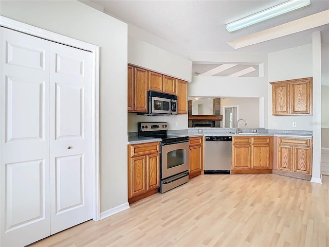 kitchen featuring stainless steel appliances, vaulted ceiling, sink, and light wood-type flooring