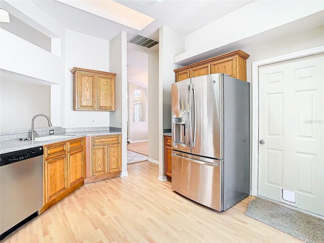 kitchen with appliances with stainless steel finishes, light stone countertops, sink, and light wood-type flooring