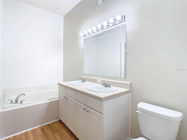 bathroom featuring vanity, wood-type flooring, tiled bath, and toilet