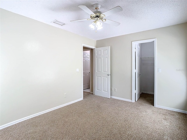 unfurnished bedroom with ceiling fan, carpet, a textured ceiling, a spacious closet, and a closet