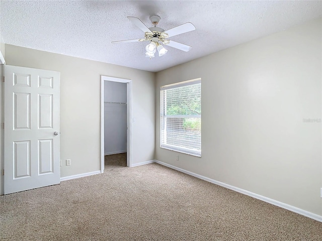unfurnished bedroom featuring a walk in closet, a textured ceiling, carpet flooring, a closet, and ceiling fan