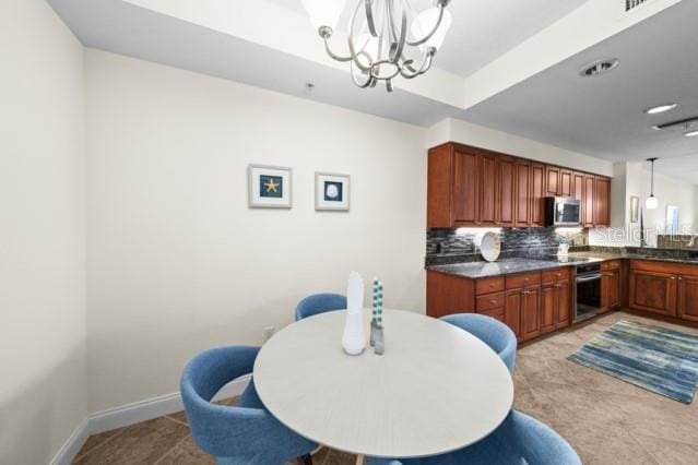 tiled dining area featuring a notable chandelier and a raised ceiling