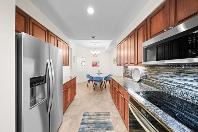 kitchen with appliances with stainless steel finishes, tasteful backsplash, dark stone countertops, light tile floors, and a chandelier