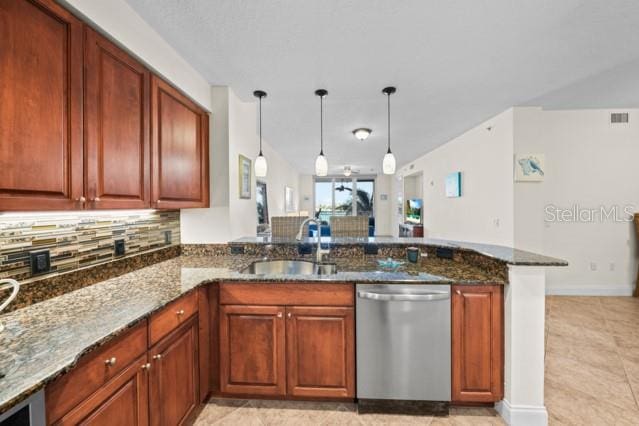 kitchen with stainless steel dishwasher, light tile flooring, dark stone countertops, decorative light fixtures, and kitchen peninsula