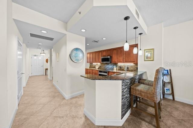 kitchen with a breakfast bar, dark stone countertops, kitchen peninsula, pendant lighting, and backsplash