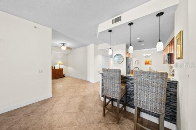 kitchen featuring light tile floors, a notable chandelier, decorative light fixtures, and stainless steel refrigerator