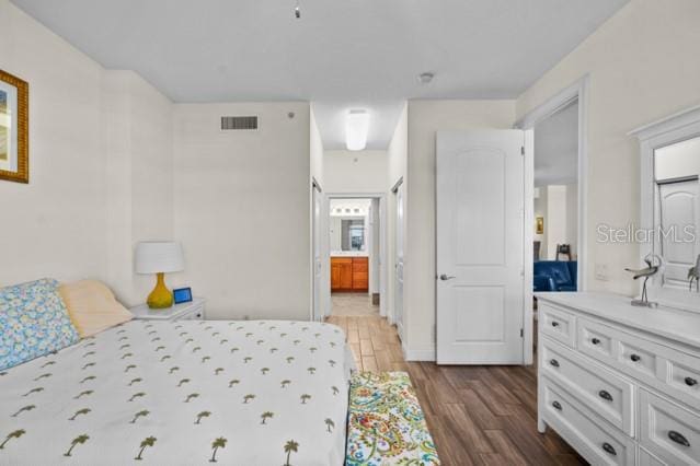 bedroom with ensuite bathroom and dark wood-type flooring