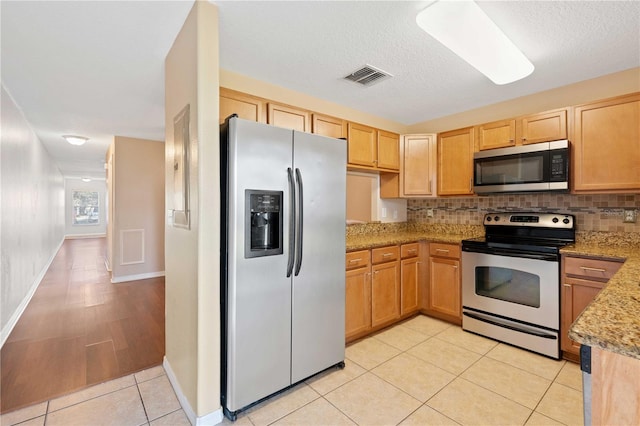 kitchen with light tile patterned flooring, tasteful backsplash, light stone counters, and appliances with stainless steel finishes