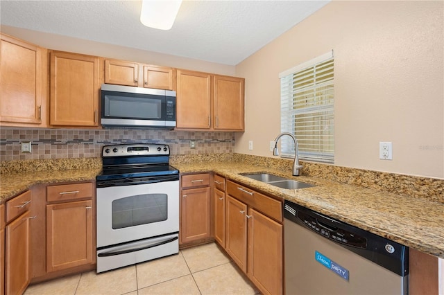 kitchen with sink, light stone counters, tasteful backsplash, light tile patterned floors, and appliances with stainless steel finishes