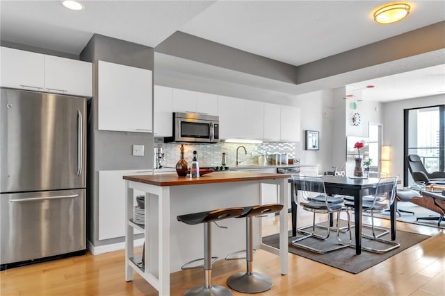 kitchen with wood counters, white cabinetry, a breakfast bar, and appliances with stainless steel finishes