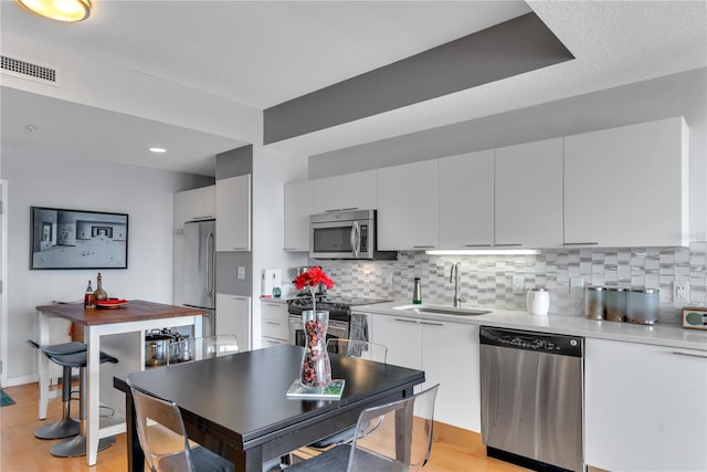 kitchen featuring sink, tasteful backsplash, light hardwood / wood-style floors, white cabinets, and appliances with stainless steel finishes