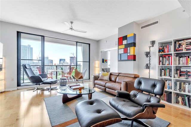 living room featuring ceiling fan, a textured ceiling, and light wood-type flooring