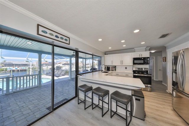 kitchen with appliances with stainless steel finishes, white cabinetry, sink, a kitchen breakfast bar, and crown molding