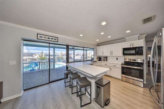 kitchen with sink, a breakfast bar area, white cabinetry, stainless steel appliances, and light hardwood / wood-style floors