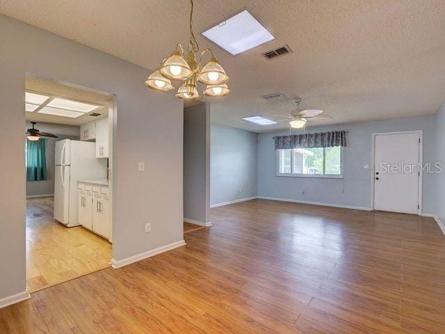 spare room featuring a textured ceiling, a skylight, ceiling fan with notable chandelier, and light wood-type flooring