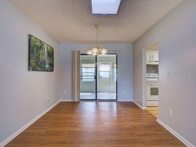 unfurnished dining area with wood-type flooring, a textured ceiling, and an inviting chandelier