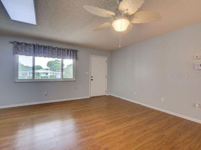 empty room with ceiling fan, wood-type flooring, a textured ceiling, and a skylight