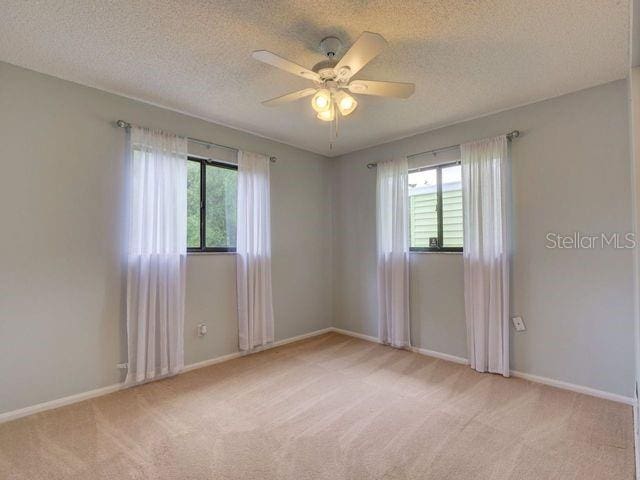 empty room with light carpet, a textured ceiling, and ceiling fan