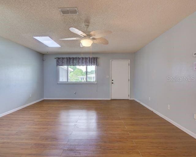 empty room featuring hardwood / wood-style flooring, ceiling fan, a textured ceiling, and a skylight