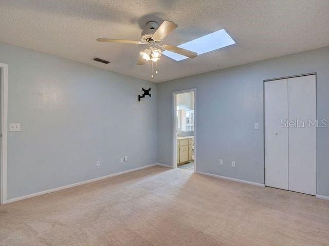 unfurnished bedroom featuring light carpet, ensuite bath, ceiling fan, a textured ceiling, and a closet