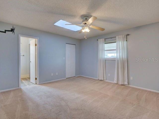 carpeted spare room with a skylight, ceiling fan, and a textured ceiling