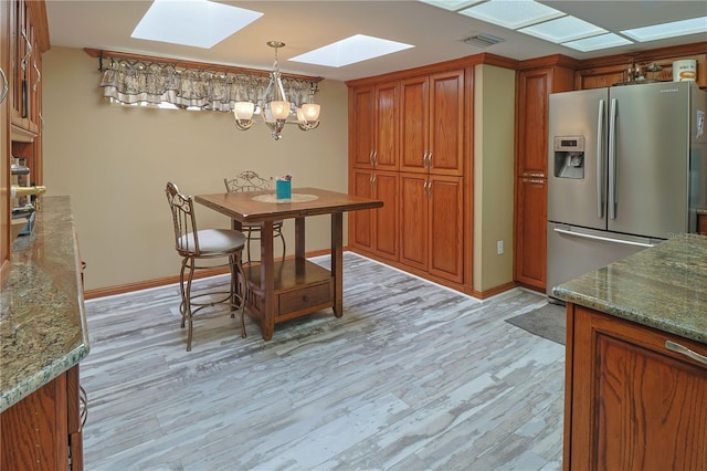 kitchen with an inviting chandelier, a skylight, dark stone counters, light hardwood / wood-style floors, and stainless steel fridge