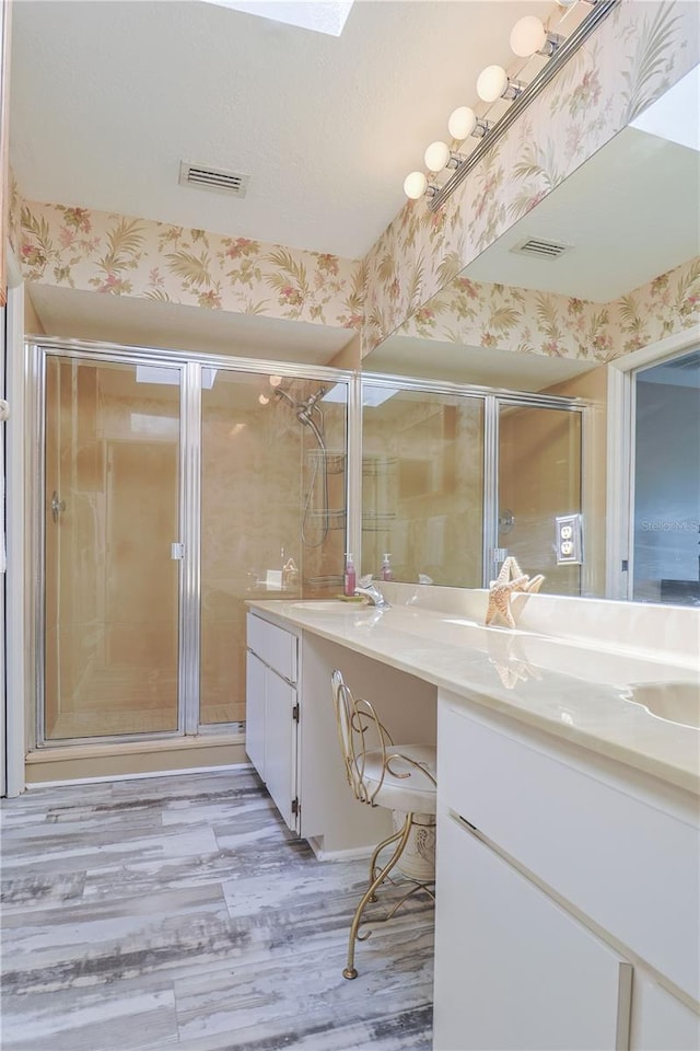 bathroom with walk in shower, hardwood / wood-style floors, vanity with extensive cabinet space, and double sink