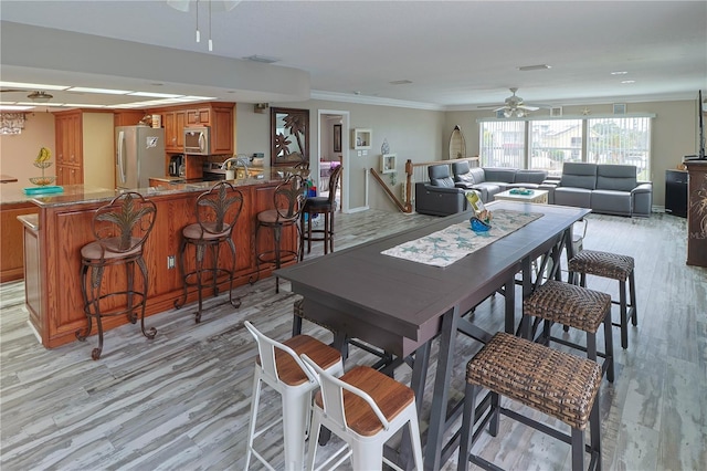 dining room featuring indoor bar, ceiling fan, light hardwood / wood-style floors, and crown molding