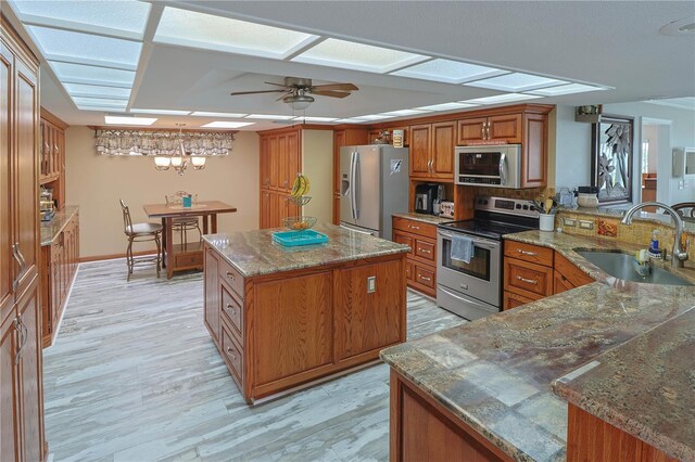 kitchen with appliances with stainless steel finishes, ceiling fan, sink, a center island, and light wood-type flooring