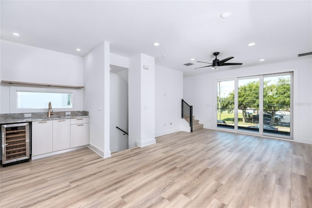 unfurnished living room with ceiling fan, light hardwood / wood-style floors, sink, and beverage cooler