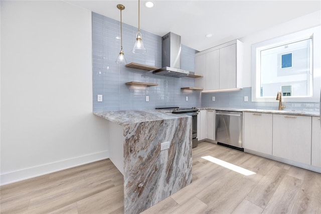 kitchen featuring stainless steel appliances, wall chimney range hood, light hardwood / wood-style floors, decorative light fixtures, and white cabinets