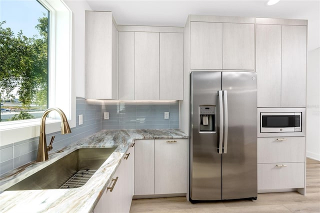 kitchen featuring sink, decorative backsplash, light stone countertops, appliances with stainless steel finishes, and light hardwood / wood-style floors