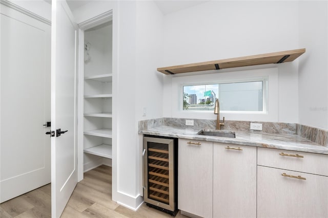 bar with light hardwood / wood-style floors, light stone countertops, sink, and wine cooler