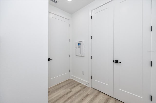 laundry area with electric panel and light hardwood / wood-style flooring