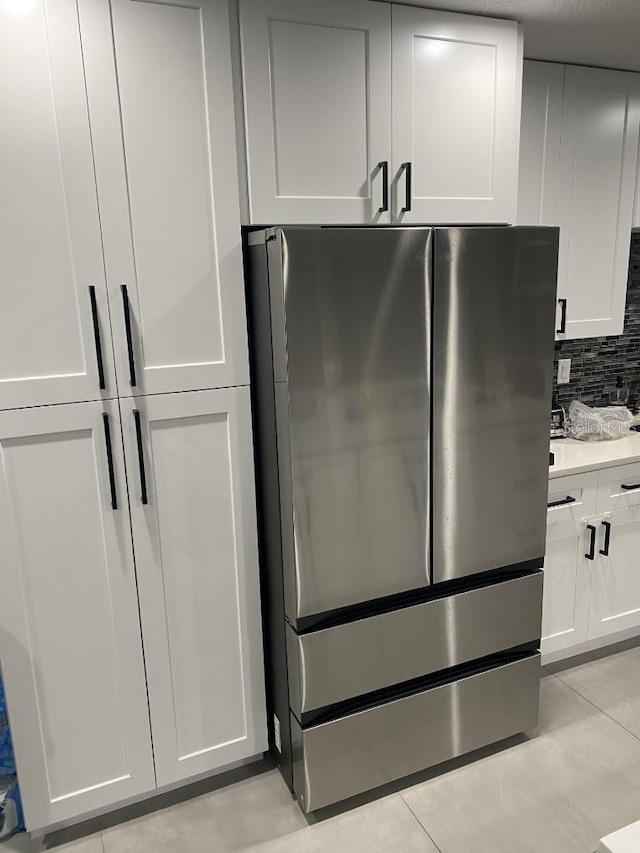 kitchen featuring white cabinets, backsplash, light tile floors, and stainless steel fridge