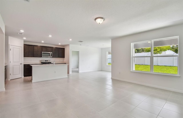 kitchen featuring appliances with stainless steel finishes, a center island with sink, light tile patterned floors, and dark brown cabinetry