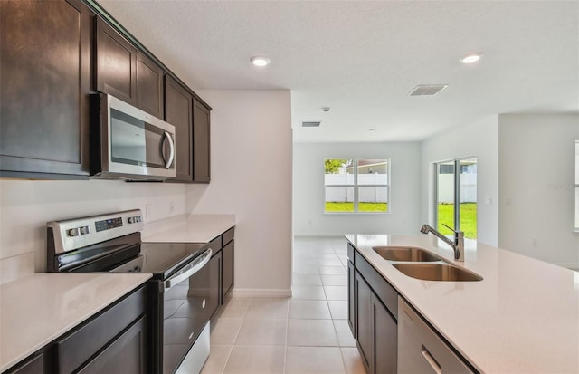 kitchen with sink, dark brown cabinetry, a textured ceiling, light tile patterned floors, and stainless steel appliances