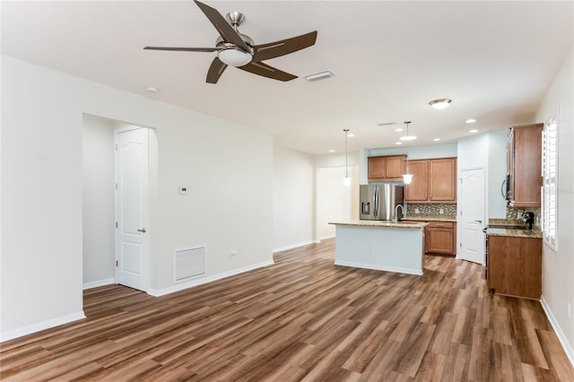 kitchen featuring dark wood-type flooring, ceiling fan, stainless steel fridge with ice dispenser, a center island with sink, and hanging light fixtures