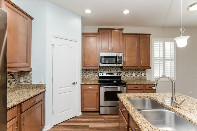 kitchen featuring appliances with stainless steel finishes, light hardwood / wood-style floors, pendant lighting, light stone countertops, and sink