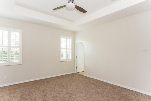 unfurnished room featuring ceiling fan, a raised ceiling, light colored carpet, and plenty of natural light