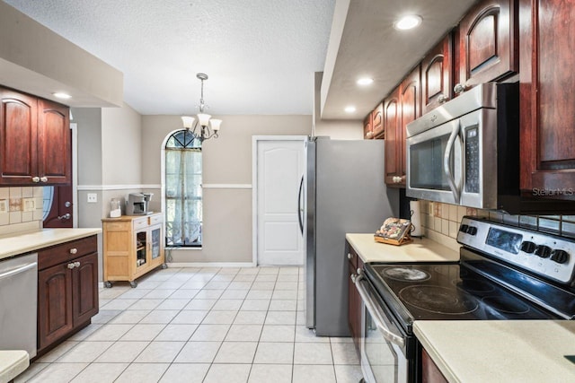 kitchen featuring backsplash, decorative light fixtures, appliances with stainless steel finishes, a notable chandelier, and light tile patterned flooring