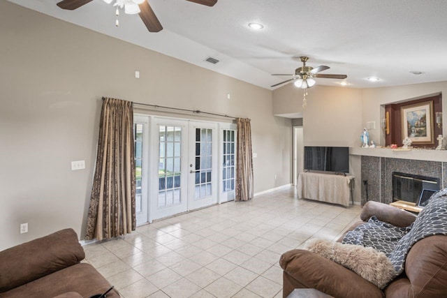 living room featuring ceiling fan, french doors, vaulted ceiling, a tiled fireplace, and light tile patterned floors