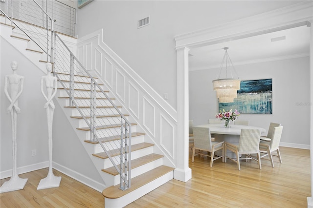 staircase featuring ornamental molding, a towering ceiling, decorative columns, and light wood-type flooring