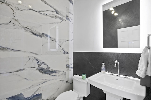 bathroom featuring toilet, tile walls, and sink