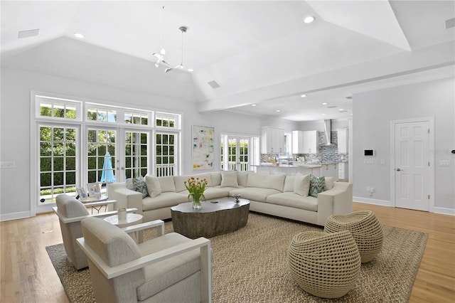 living room featuring french doors, a notable chandelier, vaulted ceiling, and light wood-type flooring