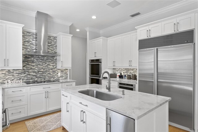 kitchen with light stone countertops, stainless steel appliances, wall chimney exhaust hood, sink, and light wood-type flooring