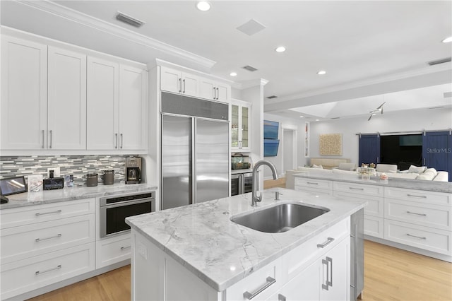 kitchen featuring a kitchen island with sink, stainless steel appliances, sink, and light wood-type flooring