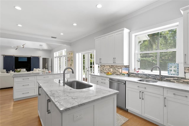 kitchen featuring white cabinetry, sink, tasteful backsplash, dishwasher, and an island with sink