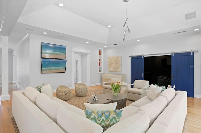 living room with light hardwood / wood-style floors, a barn door, a tray ceiling, and built in shelves