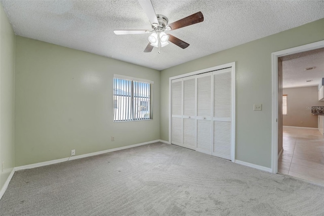 unfurnished bedroom with a textured ceiling, a closet, light colored carpet, and ceiling fan